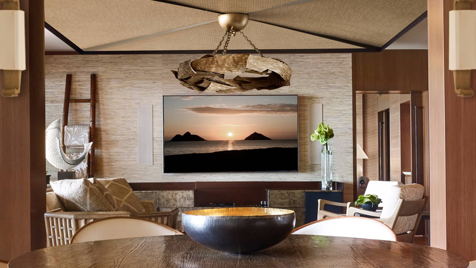 Hulopoe Presidential Suite bark chandelier over bowl on wood dining table, seating area, large TV displaying sunset