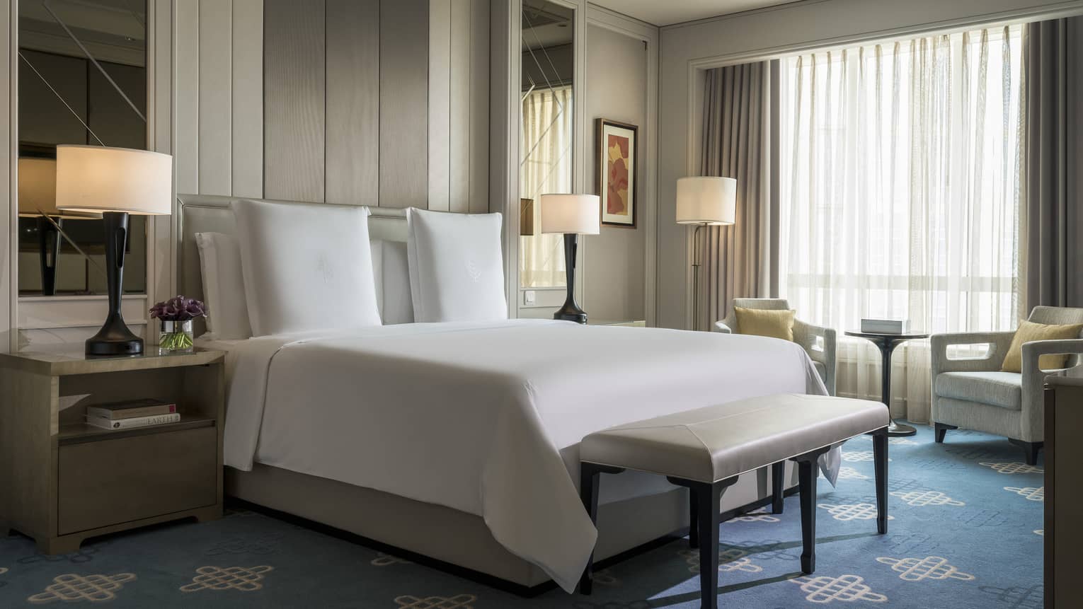 Superior Room mirrors, lamps on sides of hotel bed, bench at foot, armchairs at window