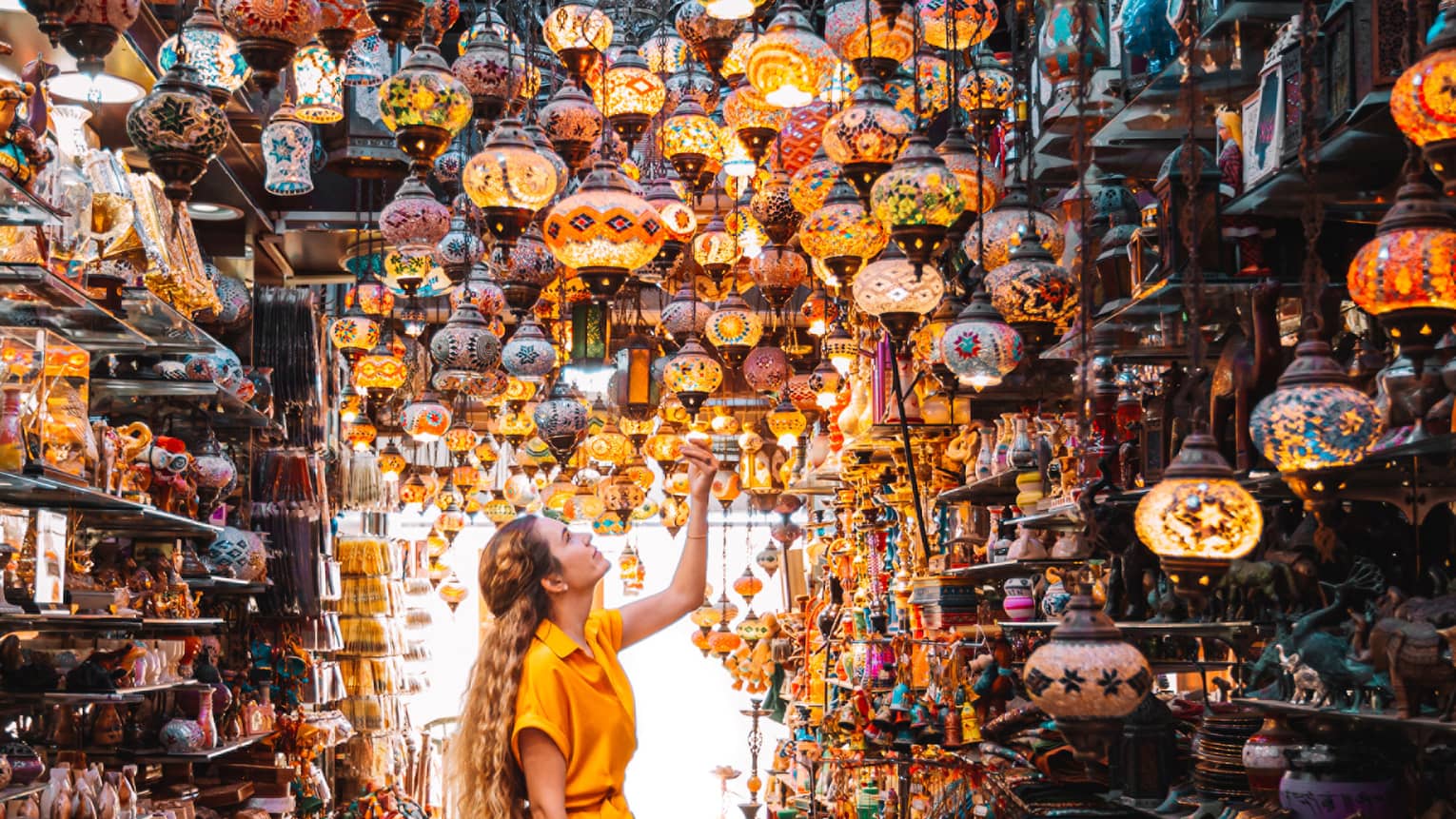 A woman in a yellow dress stands in the centre of a market under a series of bright lamps.