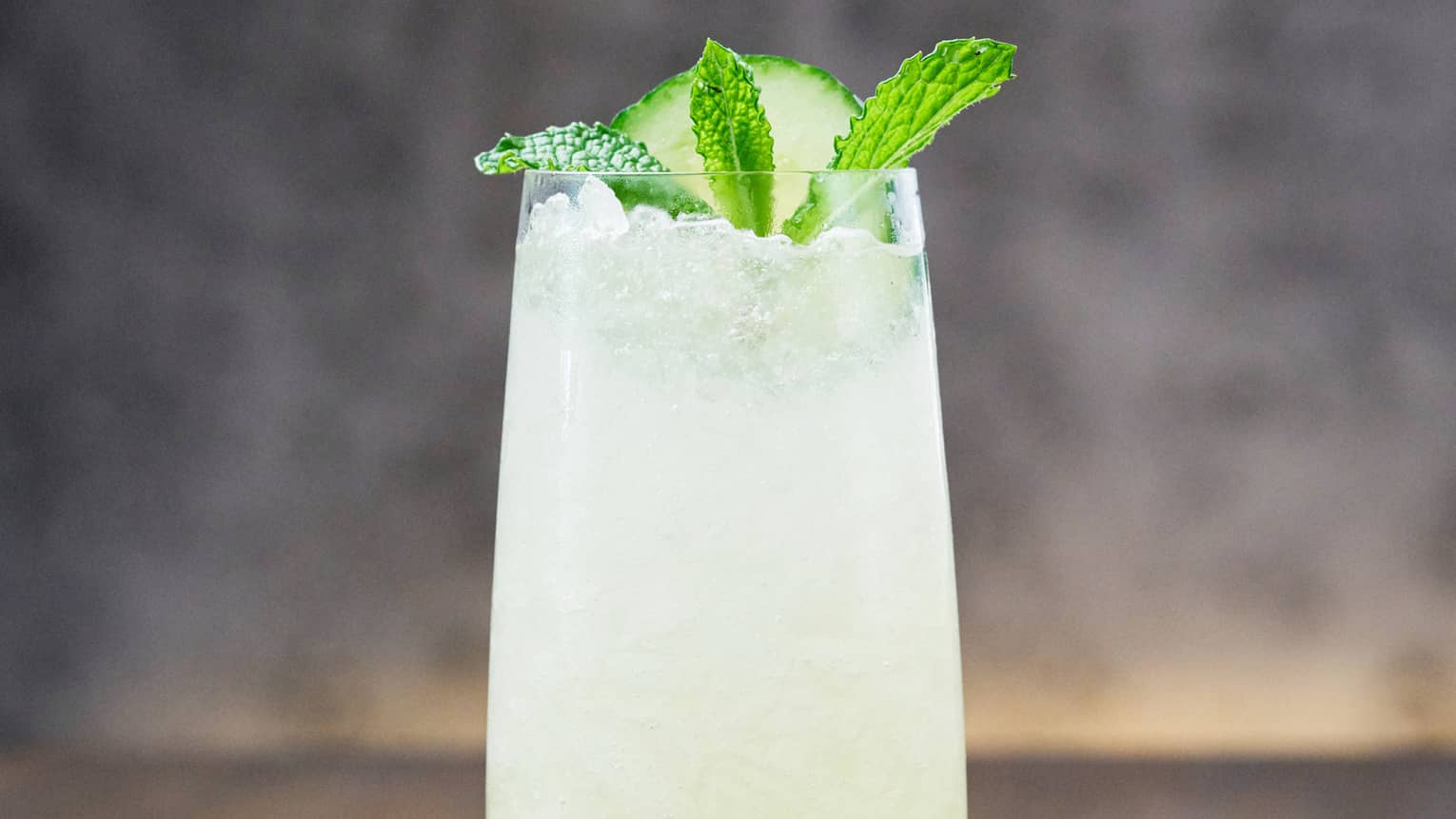 A tall cocktail that is light green in colour with a mint leaf and lime on top.