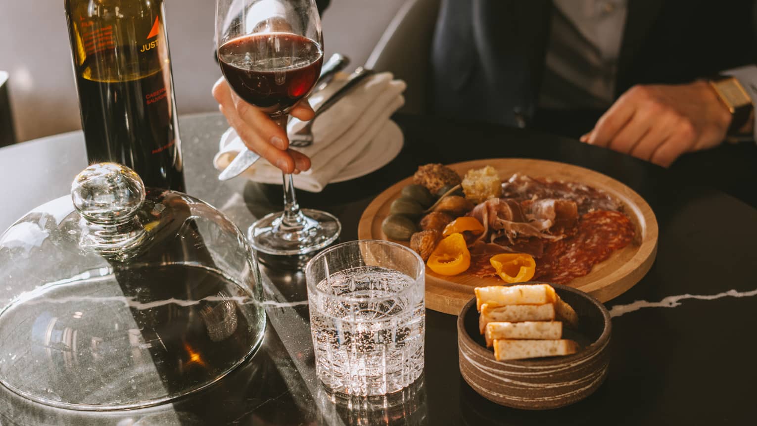 Man sits at a table with glass of red wine and charcuterie
