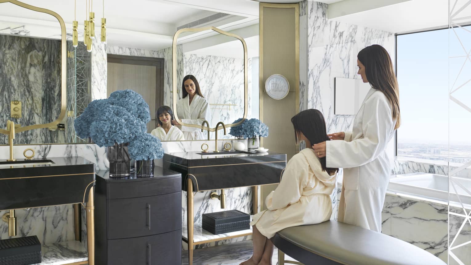 Woman and young girl in bathrobes sit in front of mirror in bathroom