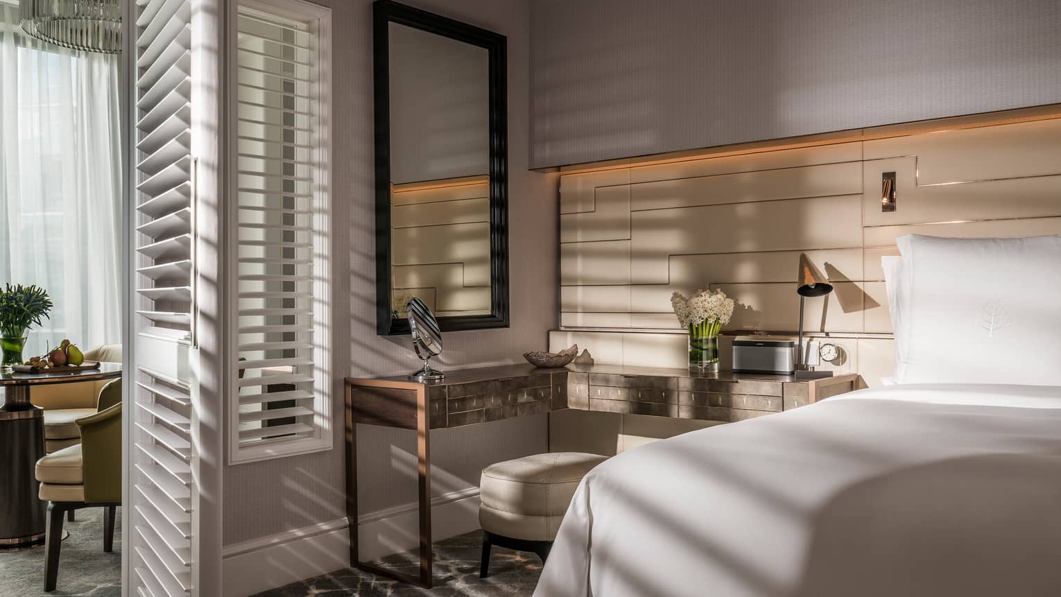 Sun streams into bedroom through tall white California shutters on dining room wall