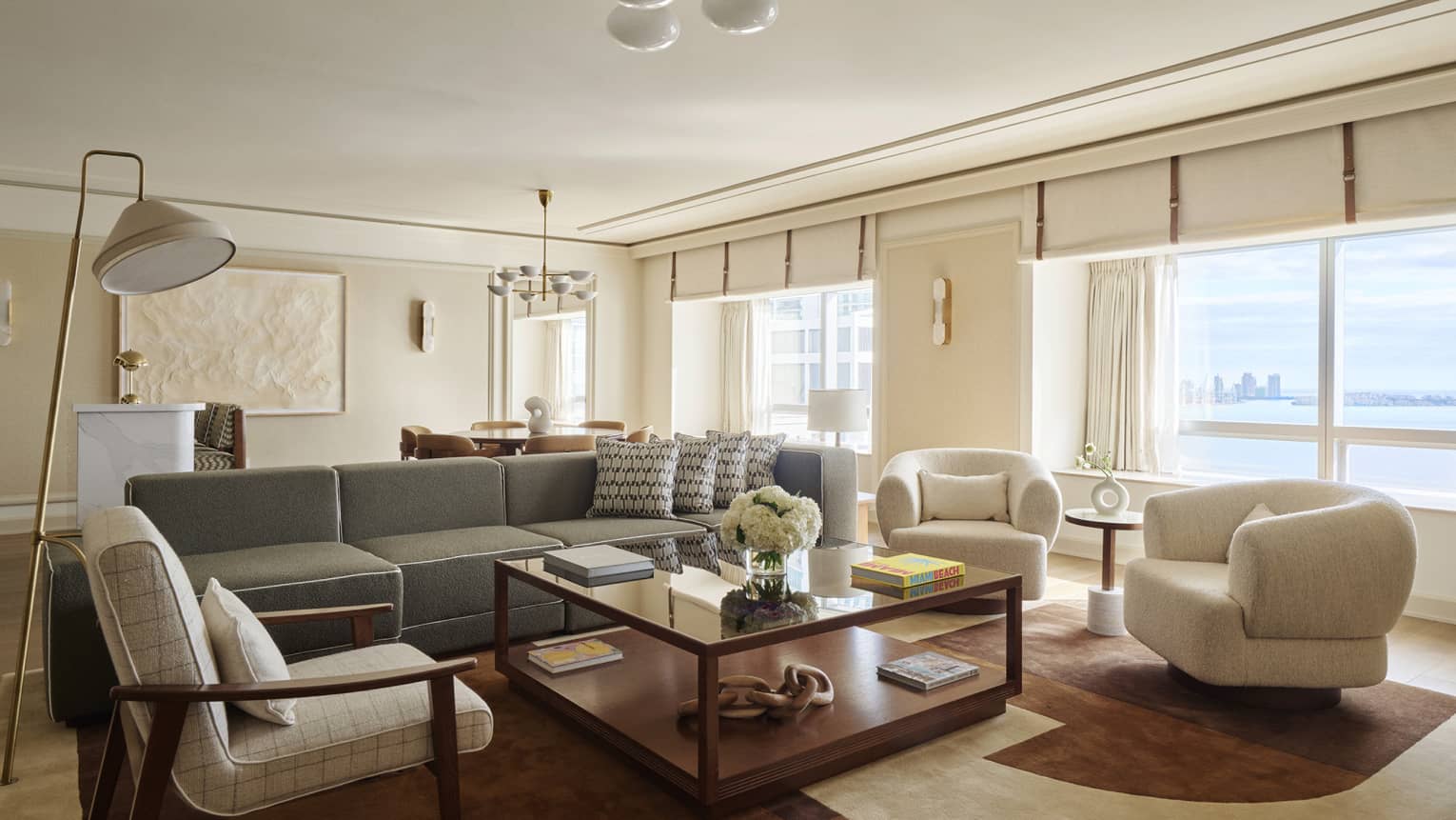 Mid-century modern living room with sofa and three arm chairs surrounding a large square coffee table, and large picture windows overlooking bay