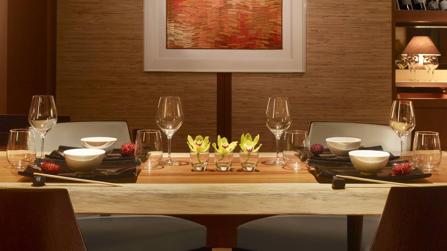 Long rustic wood private dining table with wine glasses, yellow flowers under wall with orange art