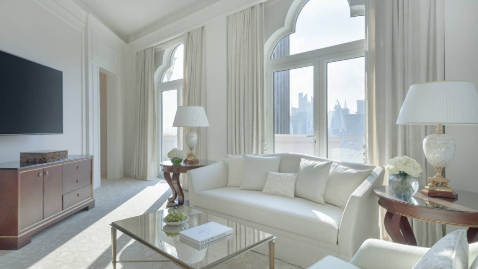 A light-filled living room with white sofa, white arm chair, tan carpet, glass coffee table, lamps