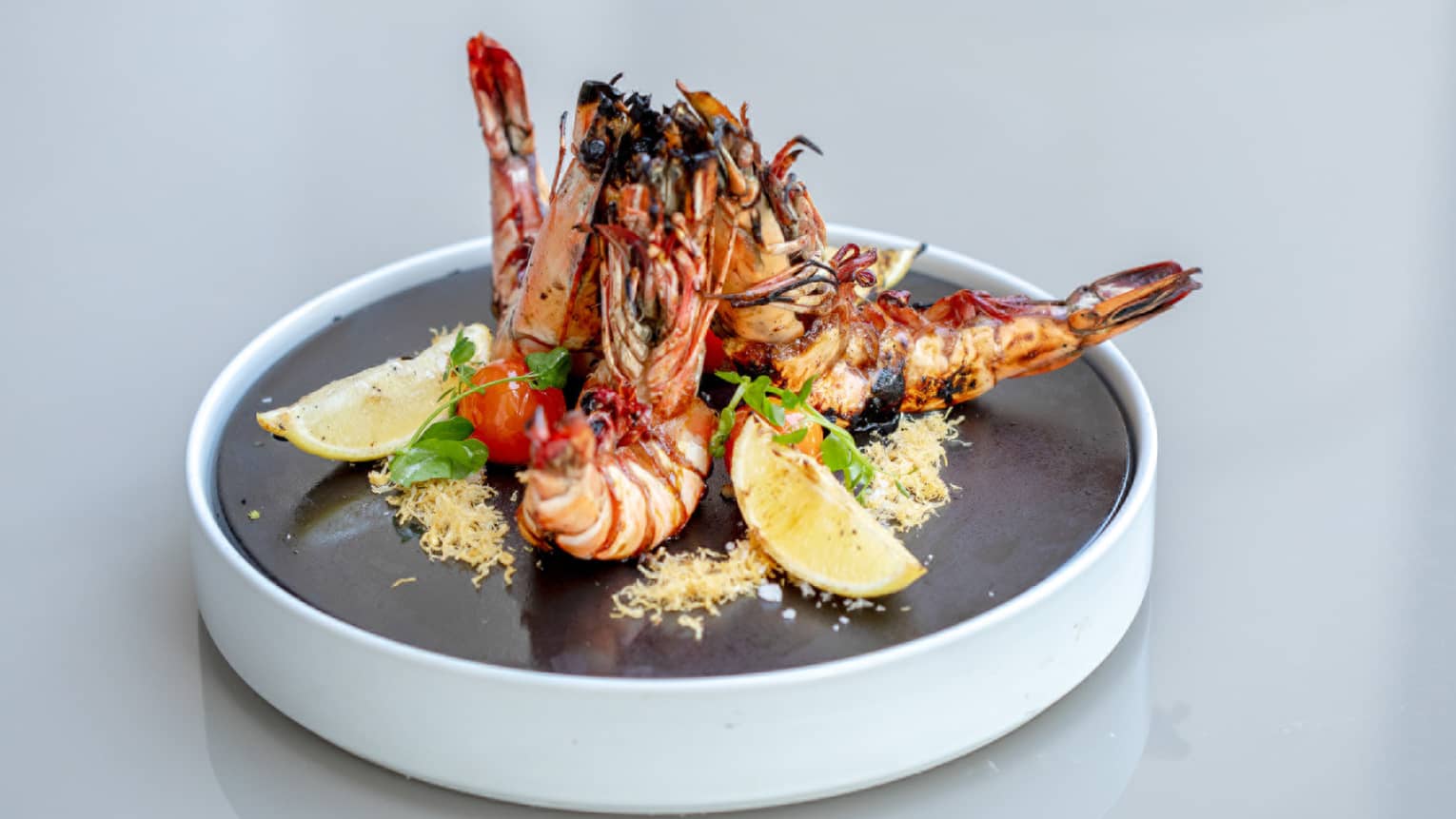 A plate of prawn with sliced lemon served on a black platter.