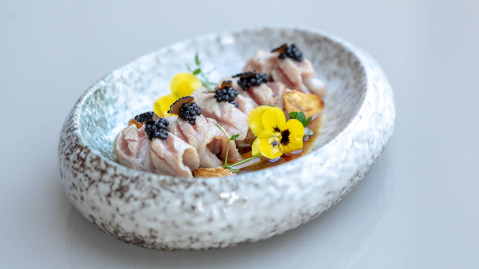 A white oval plate filled with Sashimi and yellow flowers.