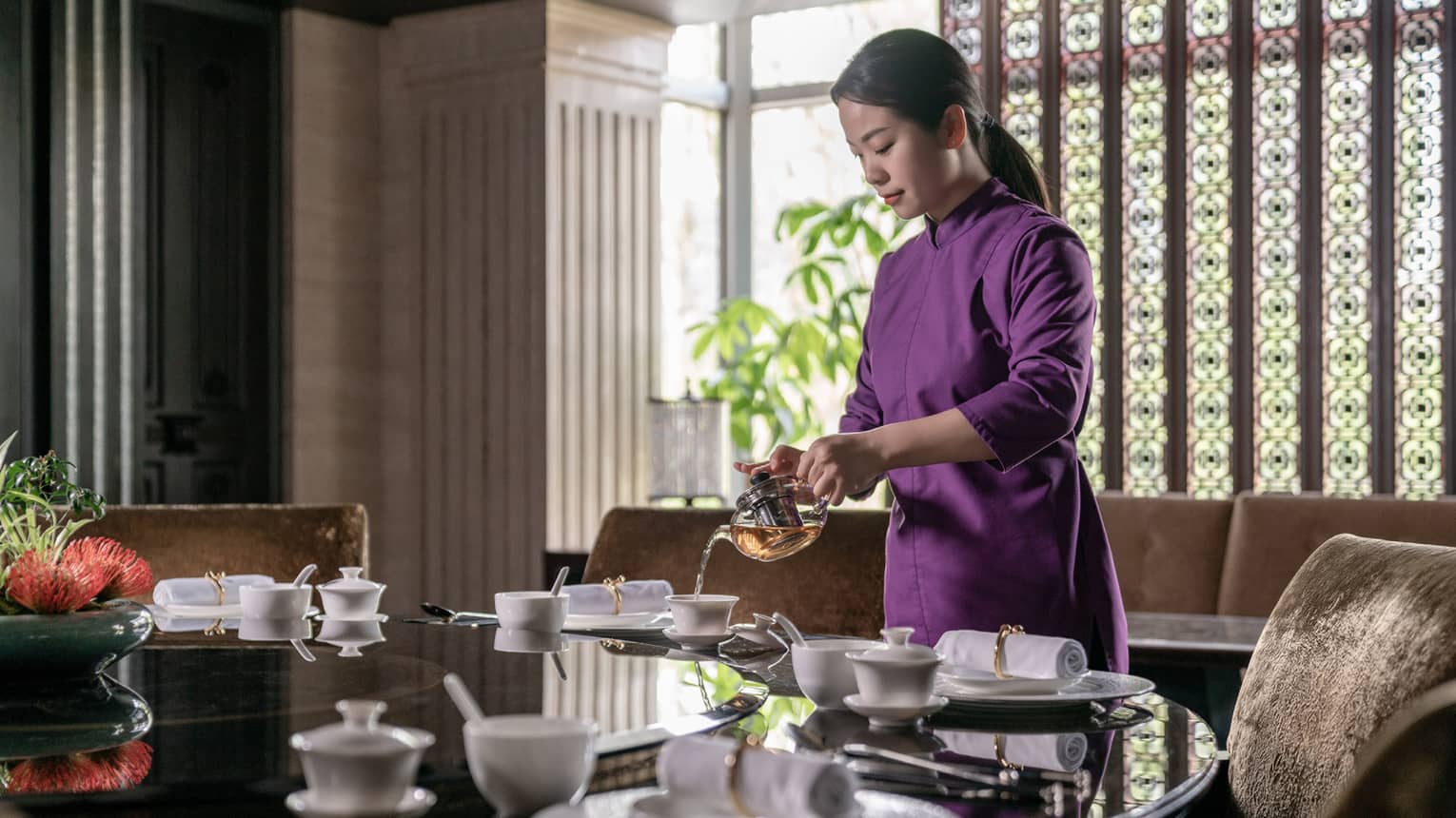 A person stands above a dining table pouring hot tea into a white mug