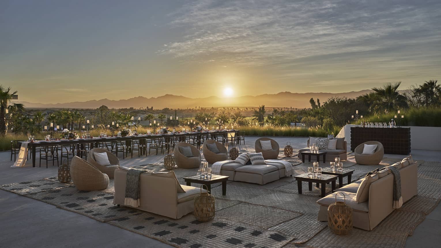 The sun sets beyond the open air ballroom terrace furnished with low cream colored couches and low dark wooden tables overlooking los cabos 