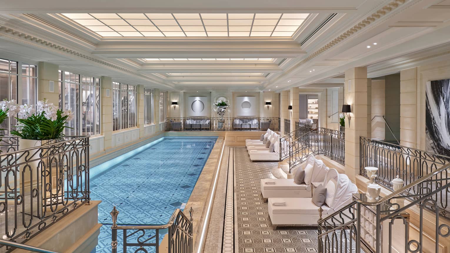 Long, elegant indoor swimming pool lined with plush white patio lounge chairs