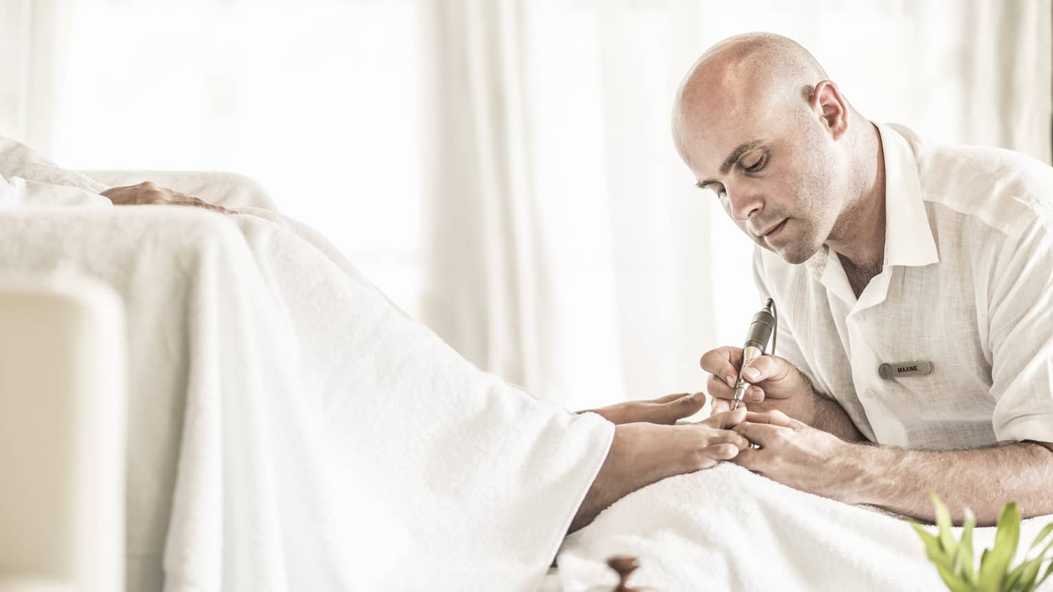 Man holds small pedicure tool at woman's feet in spa