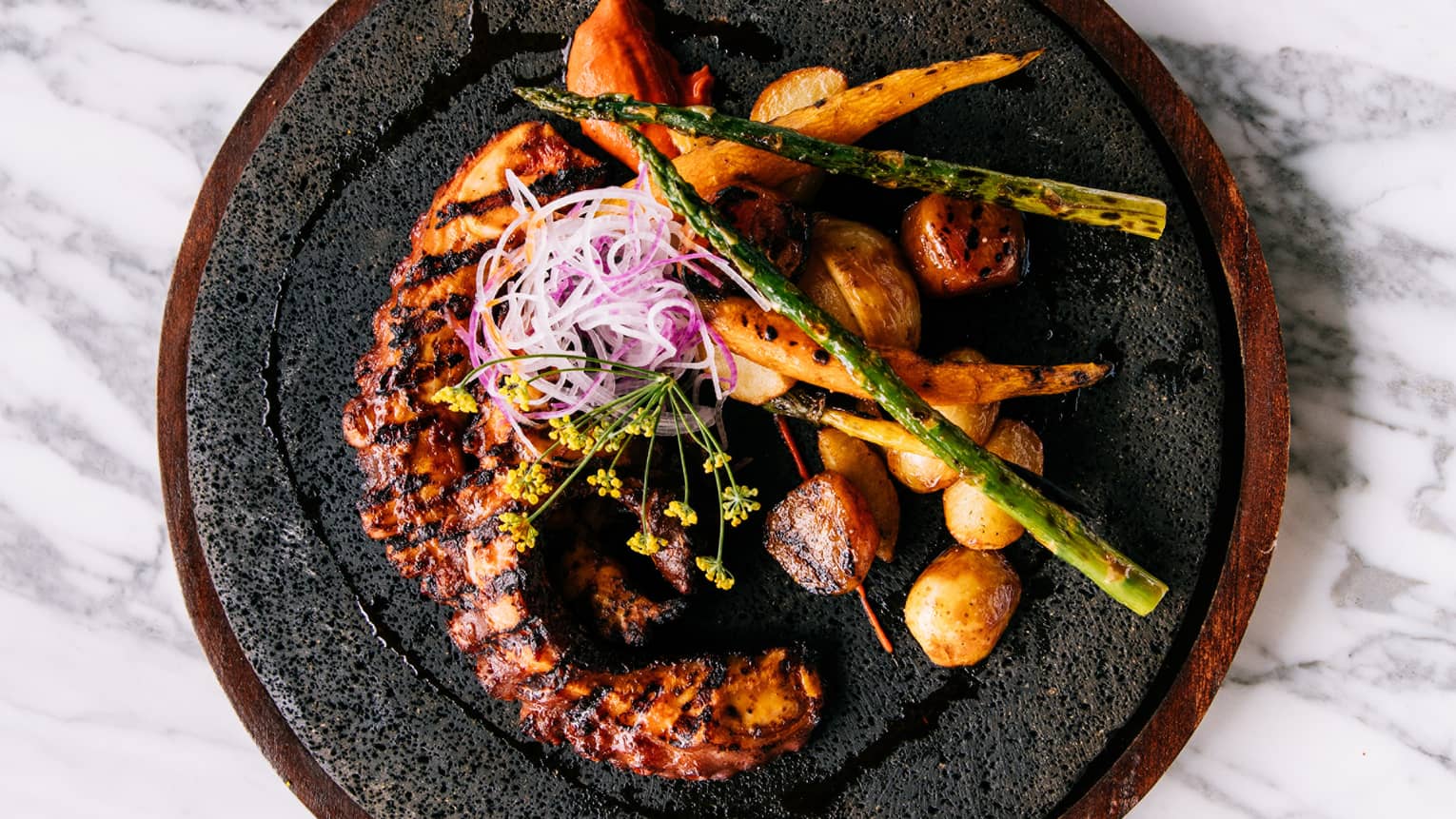 cooked octopus with potatoes and asparagus on a black plate.