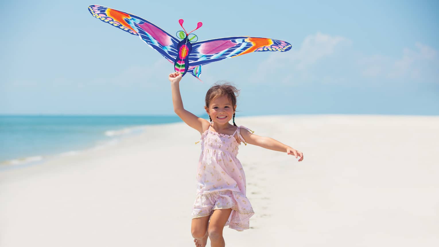 Young girl runs with colourful butterfly kite on white sand beach