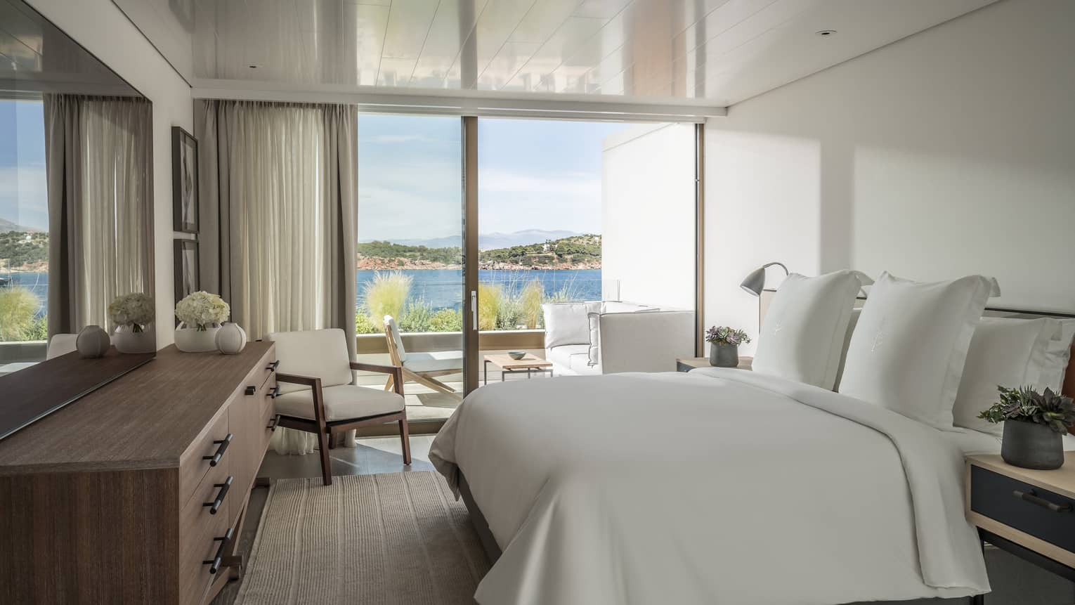 Nafsika Sea View Suite with king bed and white linens, corner arm chair, flat screen TV, sliding glass doors leading to balcony, ocean views