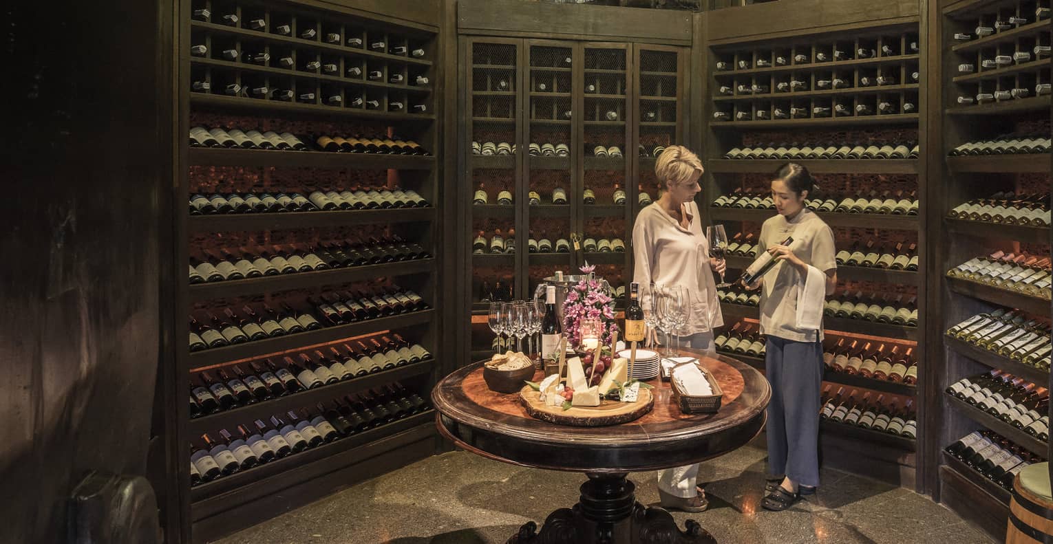 Two people examine wine bottles in Camp Wine Cellar