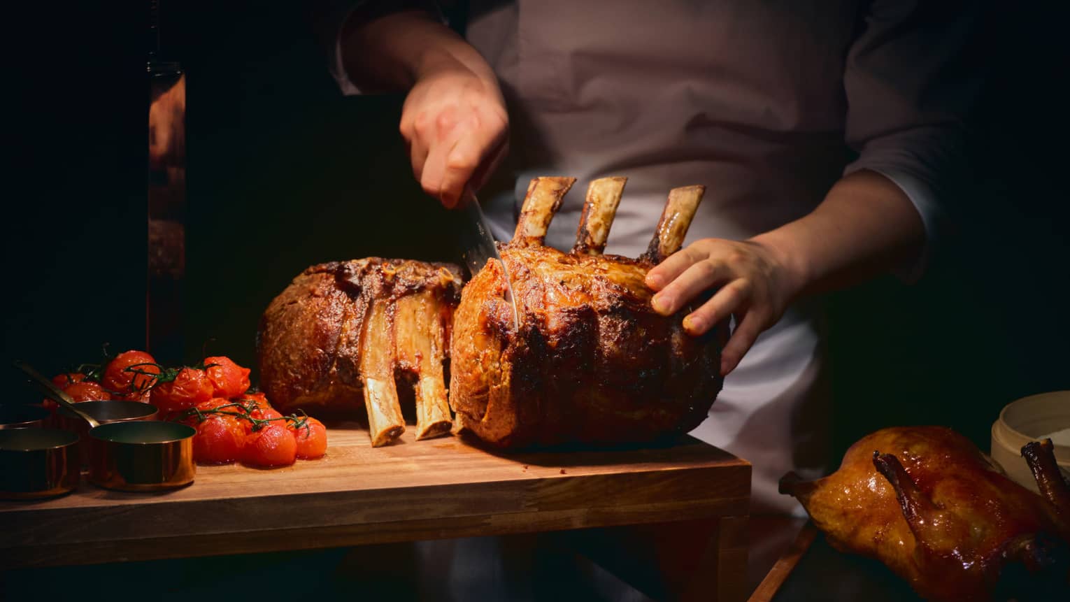 Chef slices prime rib on carving board underneath heat lamp