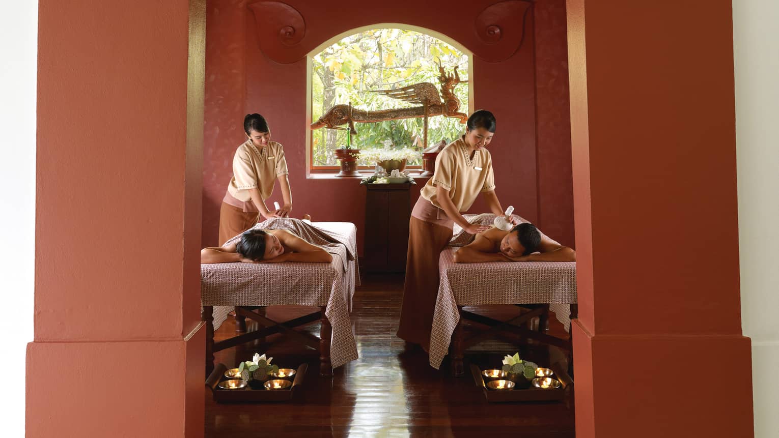 Couple lying on tables under sheets as spa staff rub their backs during Royal Heart Ritual massage