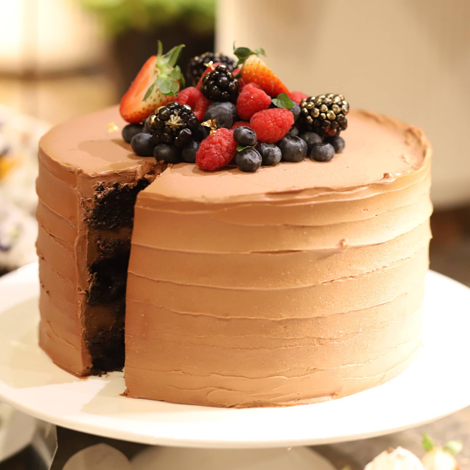 Round chocolate cake with chocolate frosting topped with fresh strawberries, blueberries, blackberries and raspberries