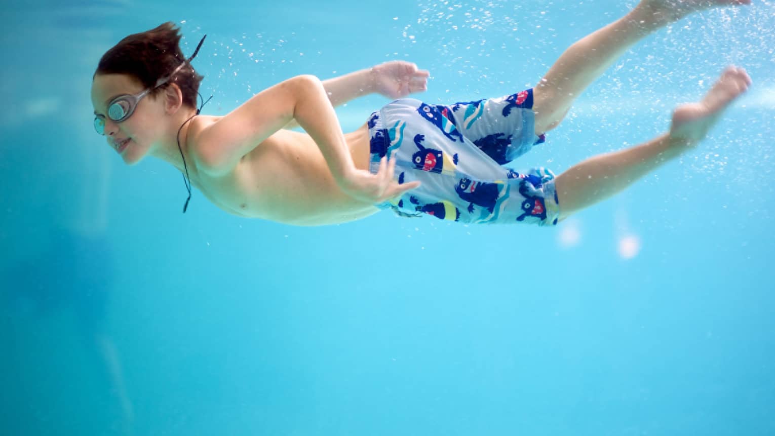 Underwater shot of a boy swimming in a pool with goggles and swim trunks