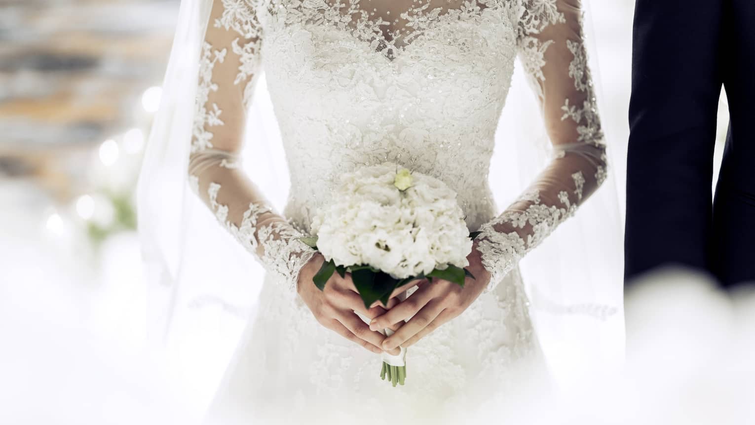 Close up of bride wearing white lace wedding gown and holding bouquet 