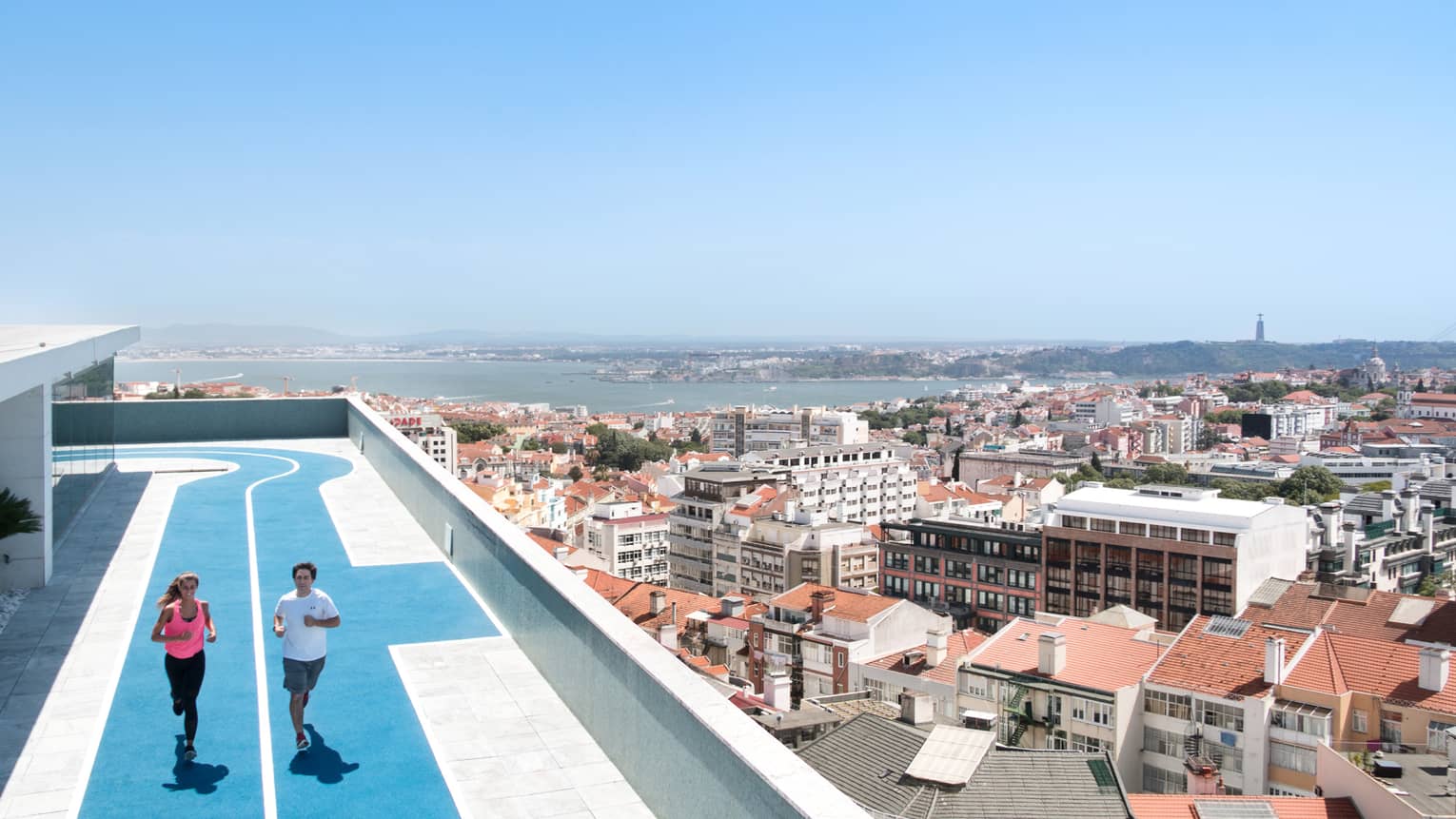 Two people run on blue, rooftop running track, overlooking Lisbon