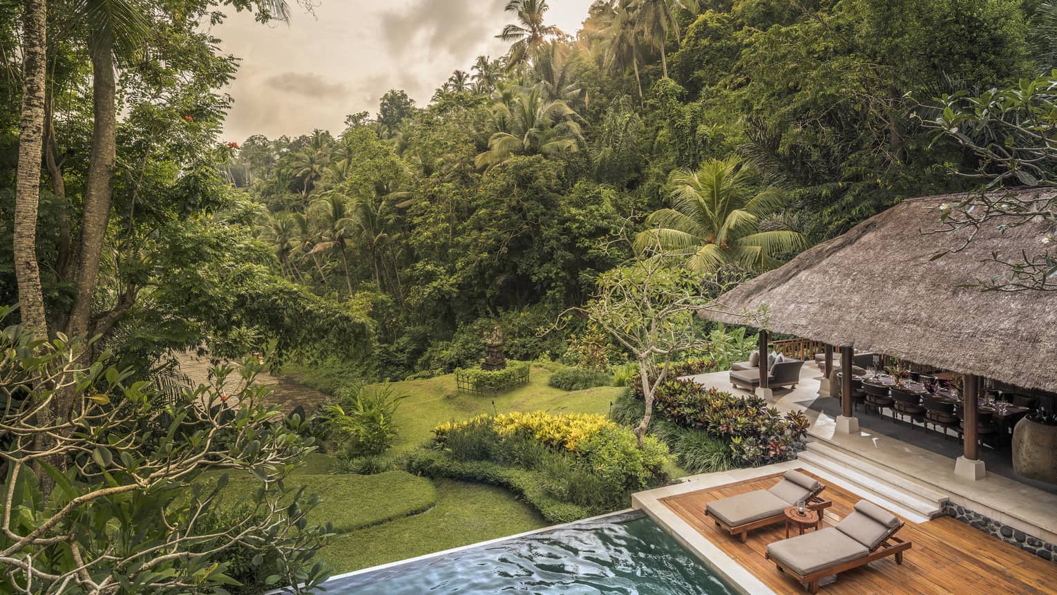 A villa with cushioned chairs and an infinity pool overlooking a river in Bali