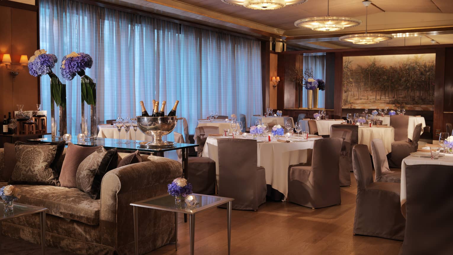 Il Teatro, plush sofa, table with Champagne bottles and flowers in front of dining tables 