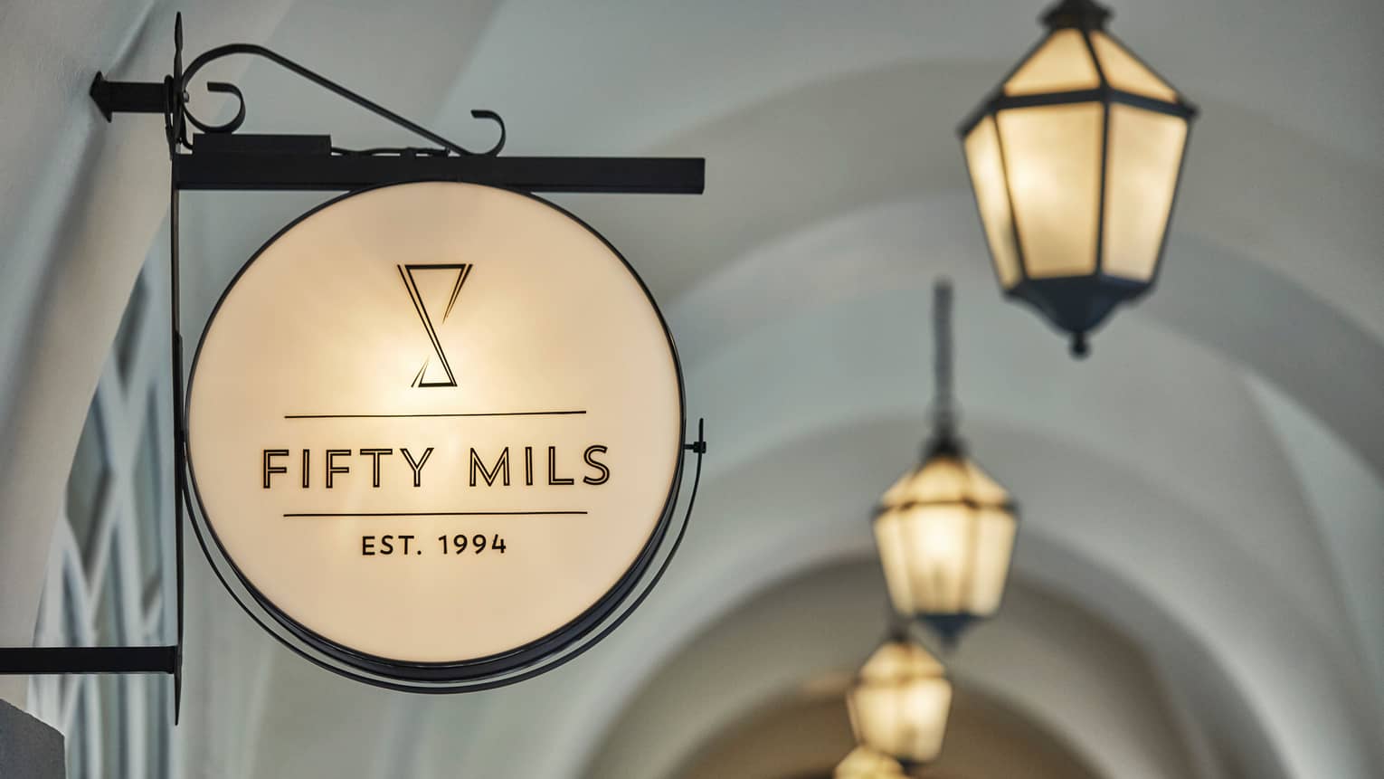 Close-up of round sign with lounge sign reading Fifty Mils Established 1994, lanterns