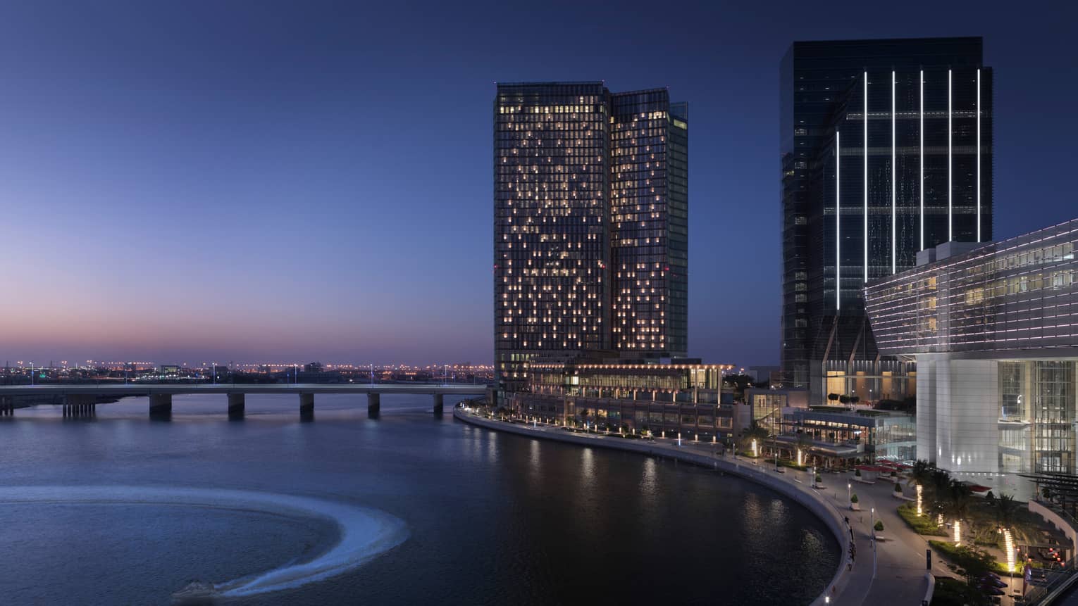 Silhouettes of high rise buildings with lights along waterfront at dusk