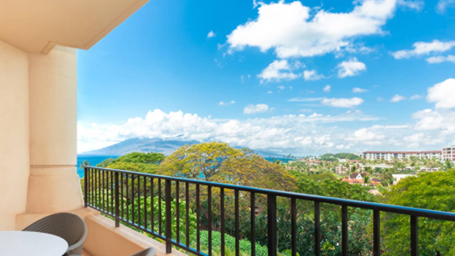 Balcony view overlooking lush greenery, distant buildings and mountain under a bright blue sky with clouds