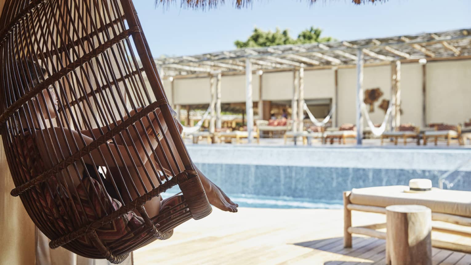 Woman sitting in hanging basket chair next to outdoor pool
