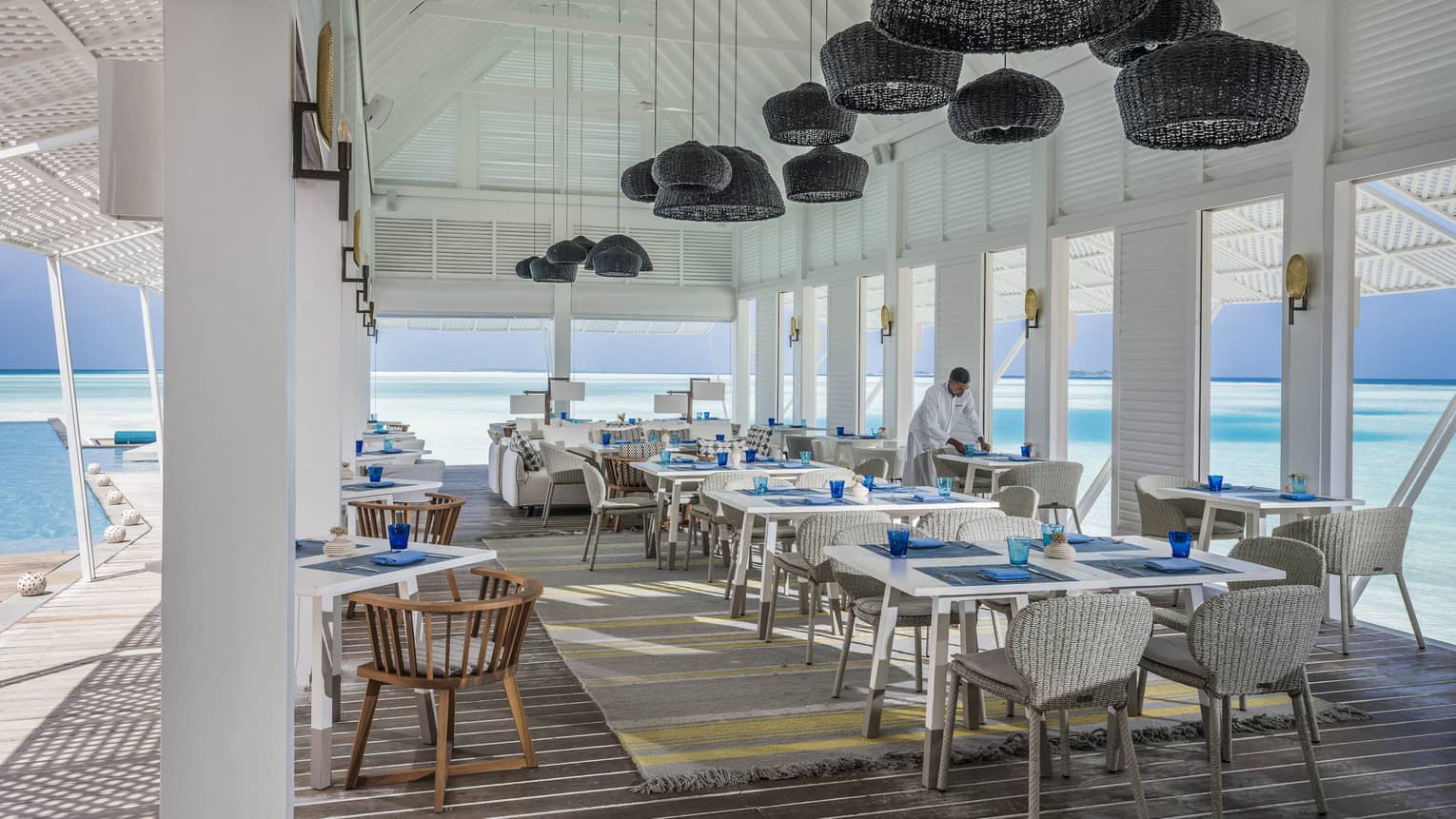 Wicker lanterns hang above clean place-settings adjacent to the ocean at the Blu Beach Club