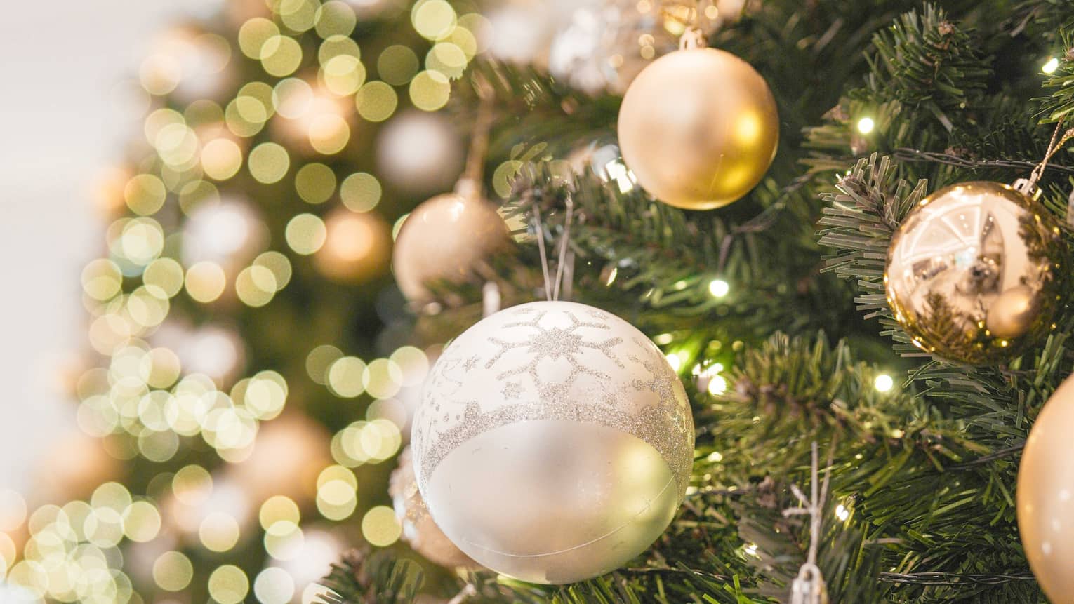 Close up of a Christmas tree with silver and gold ornaments and twinkling lights
