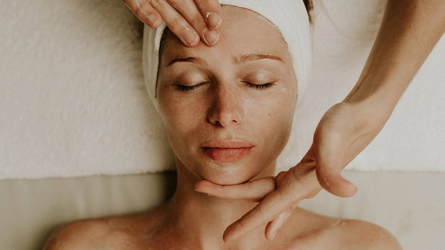 A woman reclines as a spa attendant performs a facial