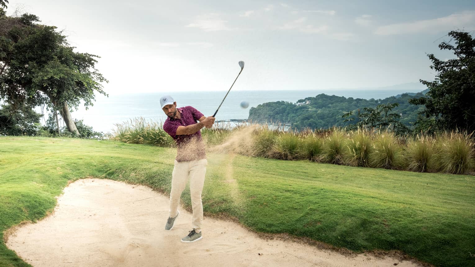 A golfer hitting a ball out of sand.