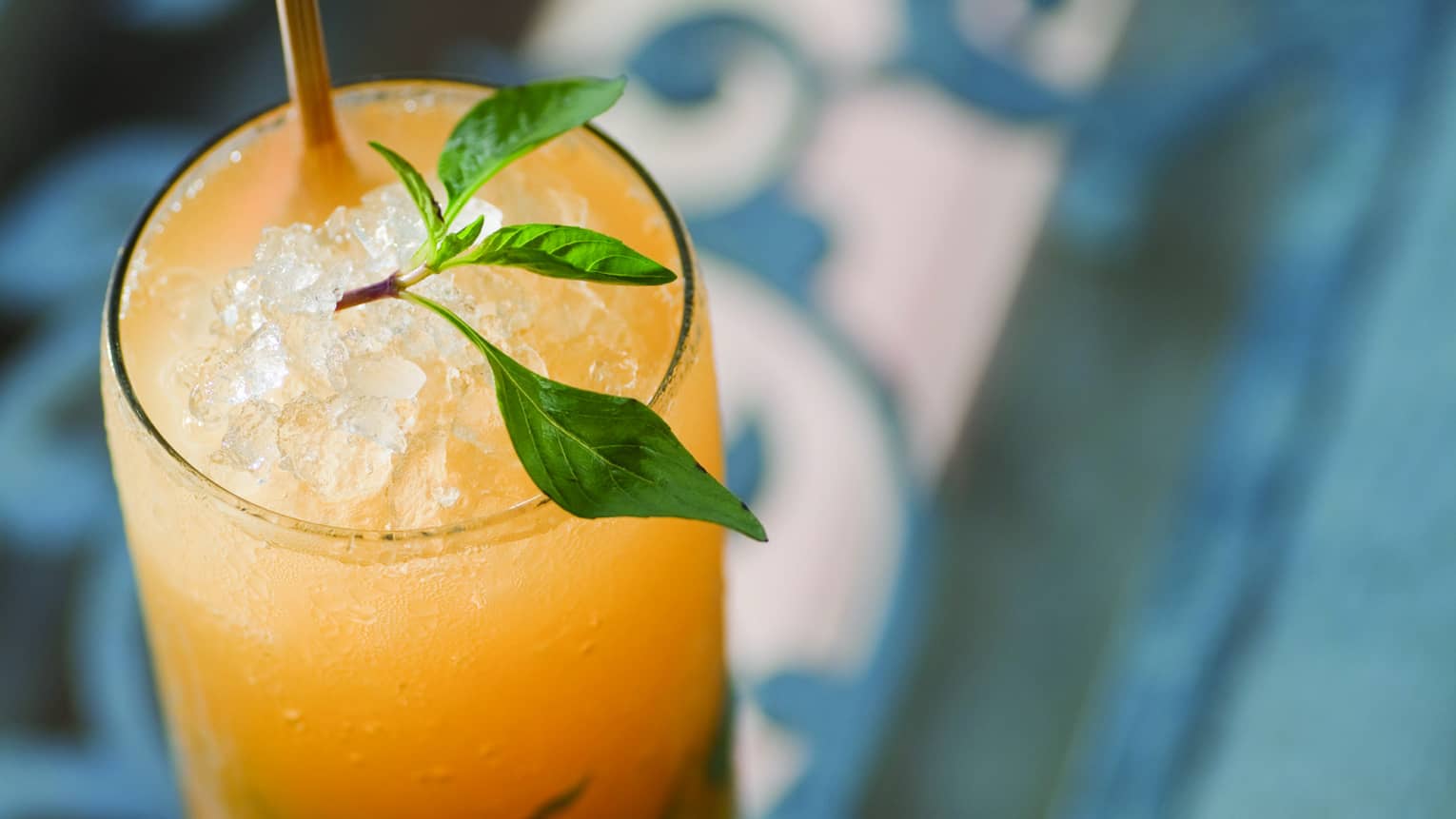 Bright yellow cocktail in tall glass with crushed ice, garnished with sprig of Thai basil