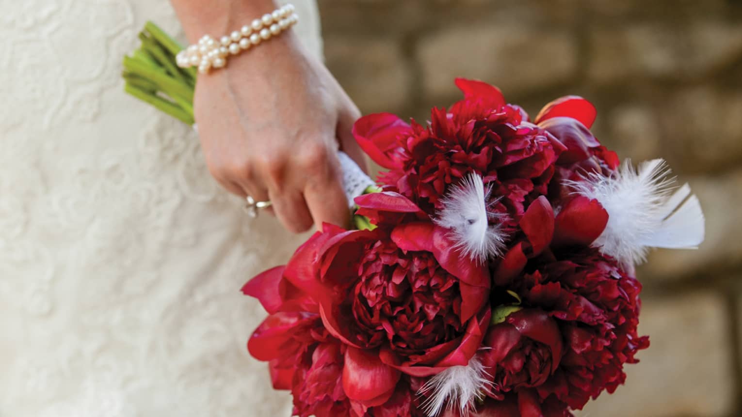 Bride wearing white wedding gown holding bouquet of red flowers