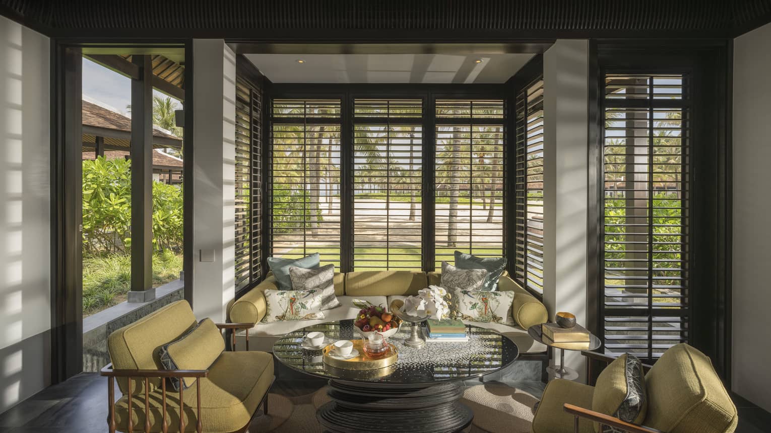Guest room living area with mustard-coloured armchairs and sofa with floor-to-ceiling windows with. beach views