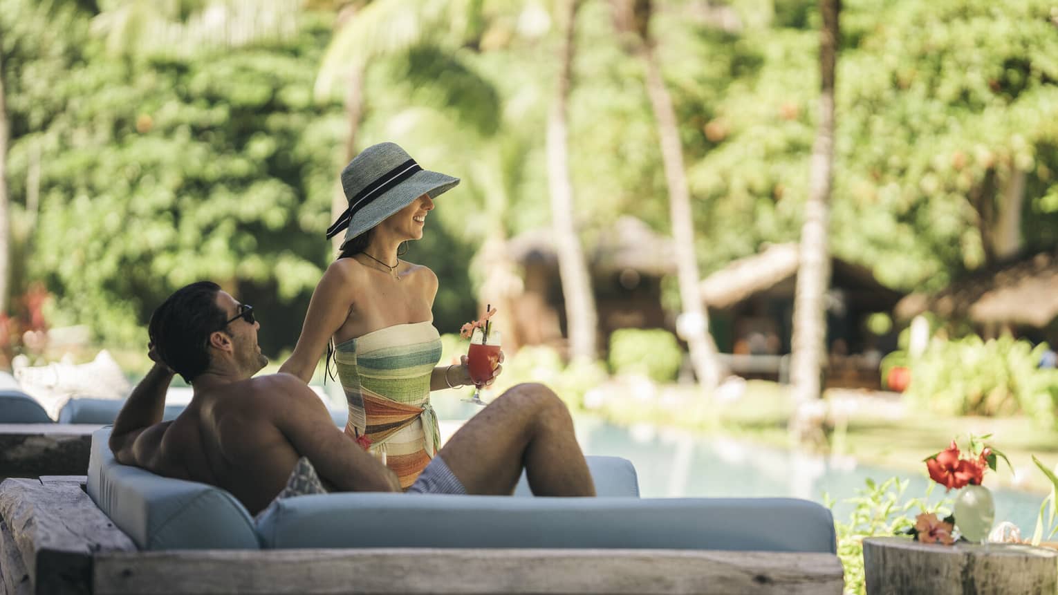 A couple drinking cocktails while lounging on an outdoor chair by a pool