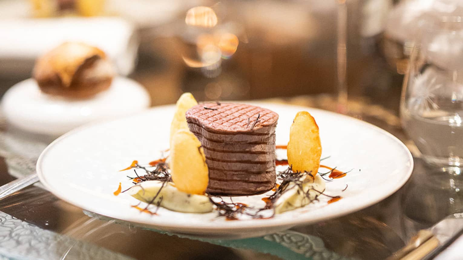 Thick grilled steak and gourmet garnishes on dining plate next to glass of red wine