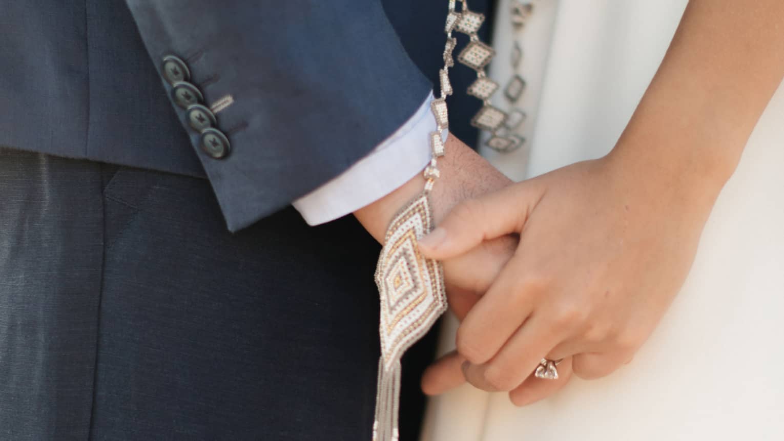 A closeup of a man and woman holding hand with a necklace or rosary hanging.