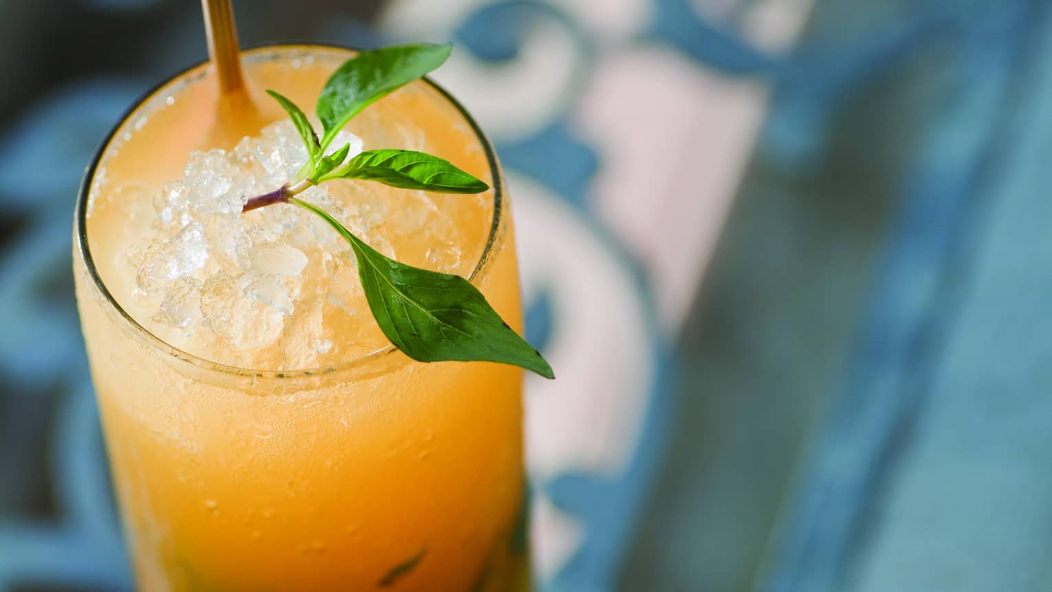 Bright yellow cocktail in tall glass with crushed ice, garnished with sprig of Thai basil