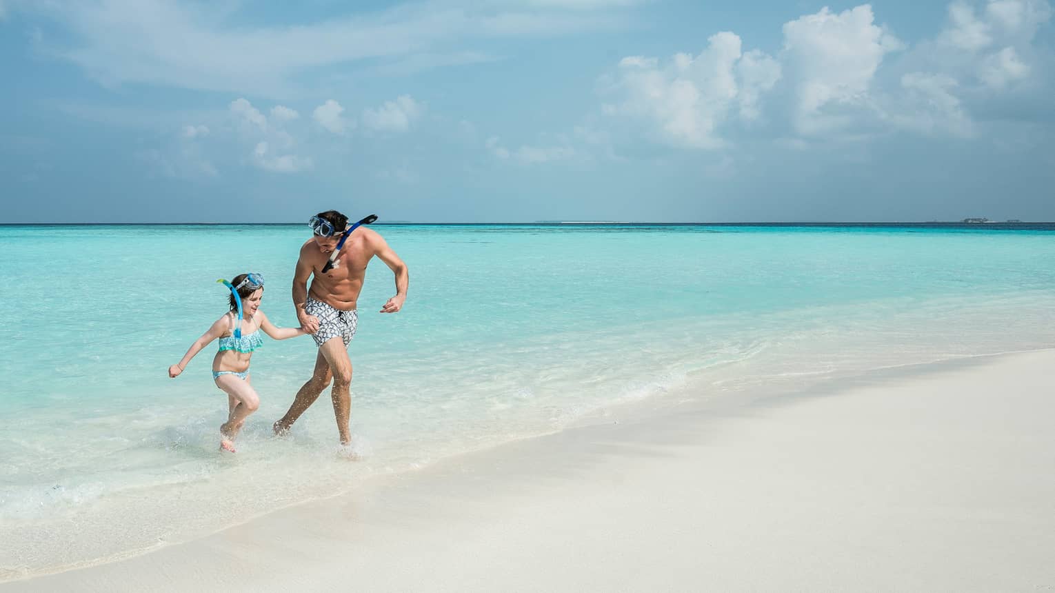 Man, young girl wearing snorkelling mask walk from blue lagoon to white sand beach