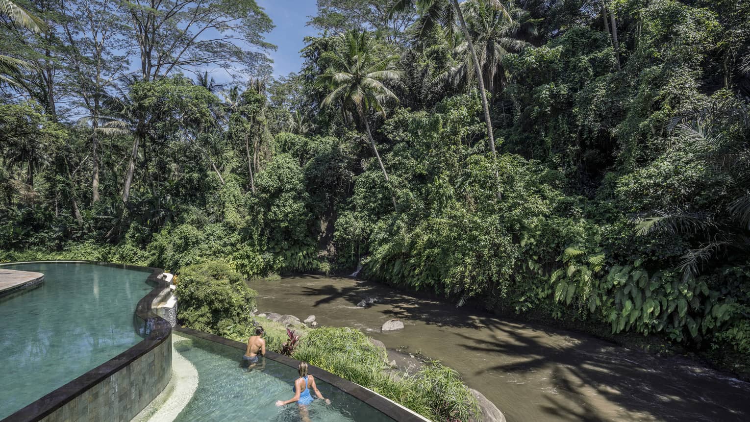 Hotel guests swimming in a pool, overlooking a river in Bali