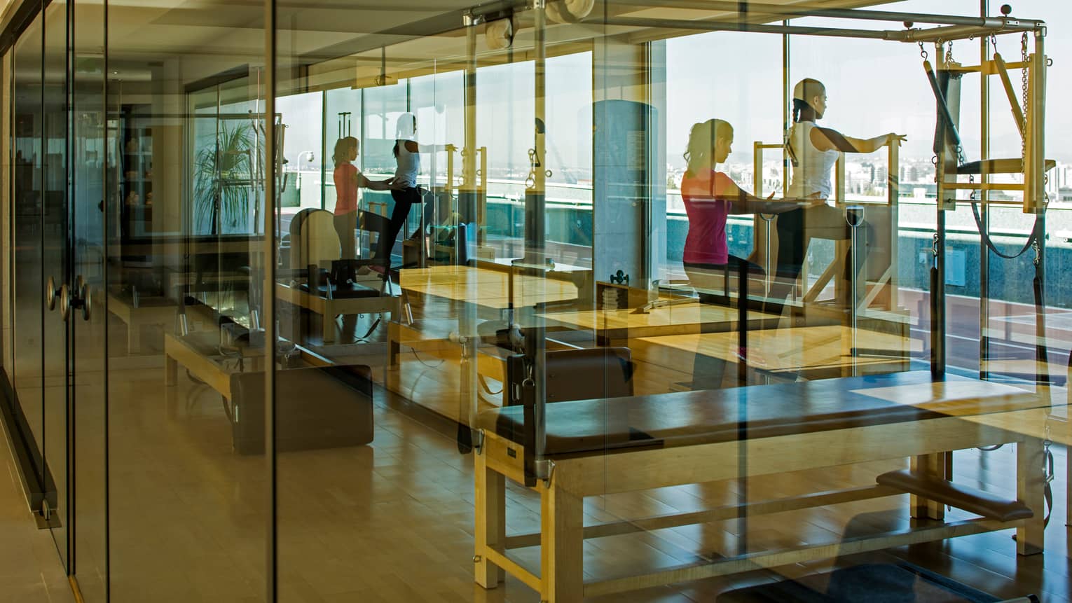 Reflections of woman climbing cardio stair climbing machine as trainer holds waist behind her, seen through glass pane