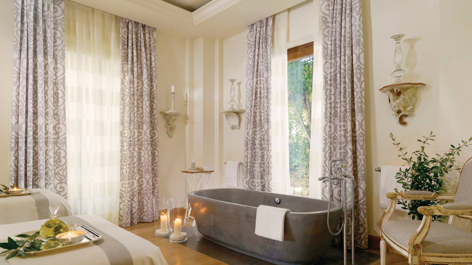 Spa couples massage beds, candles on floor by free-standing tub under tall windows