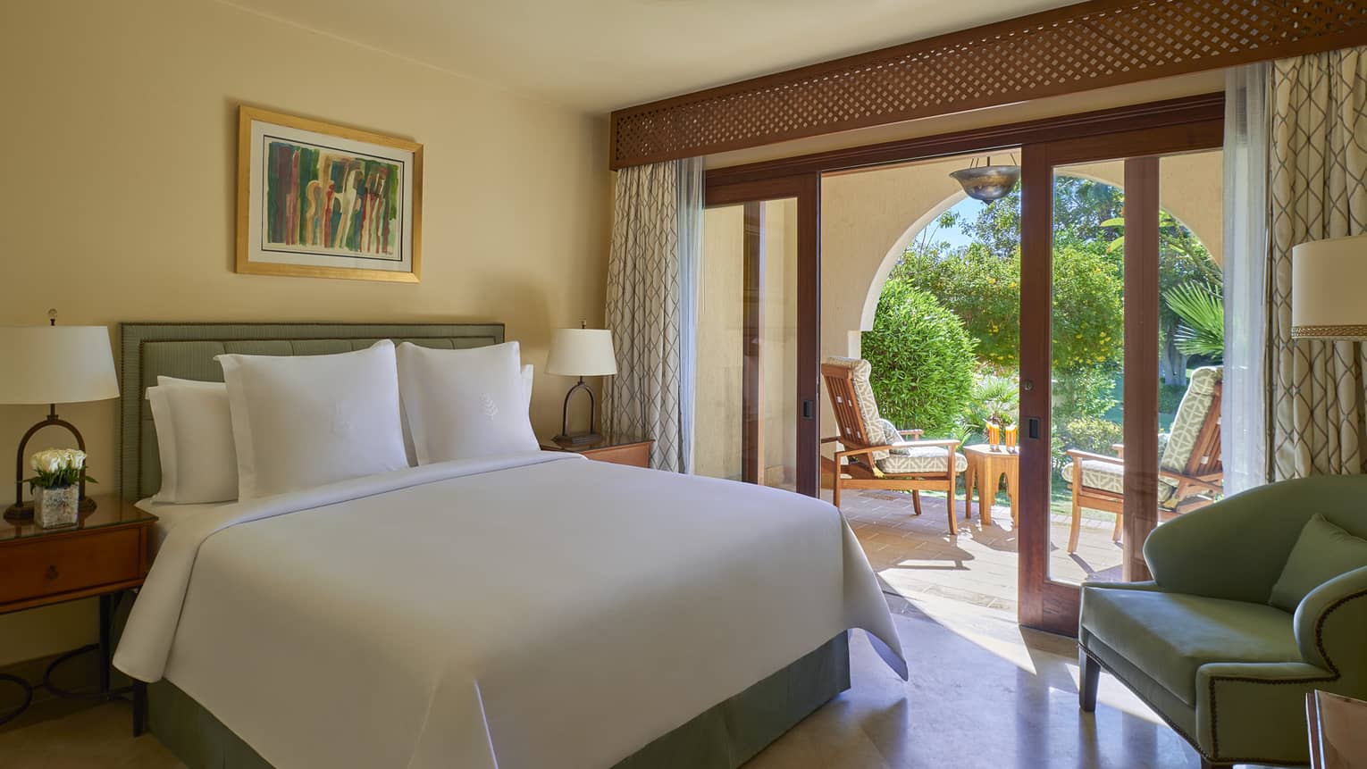 Bedroom with light yellow walls, white king bed, light blue armchair and walk-out terrace