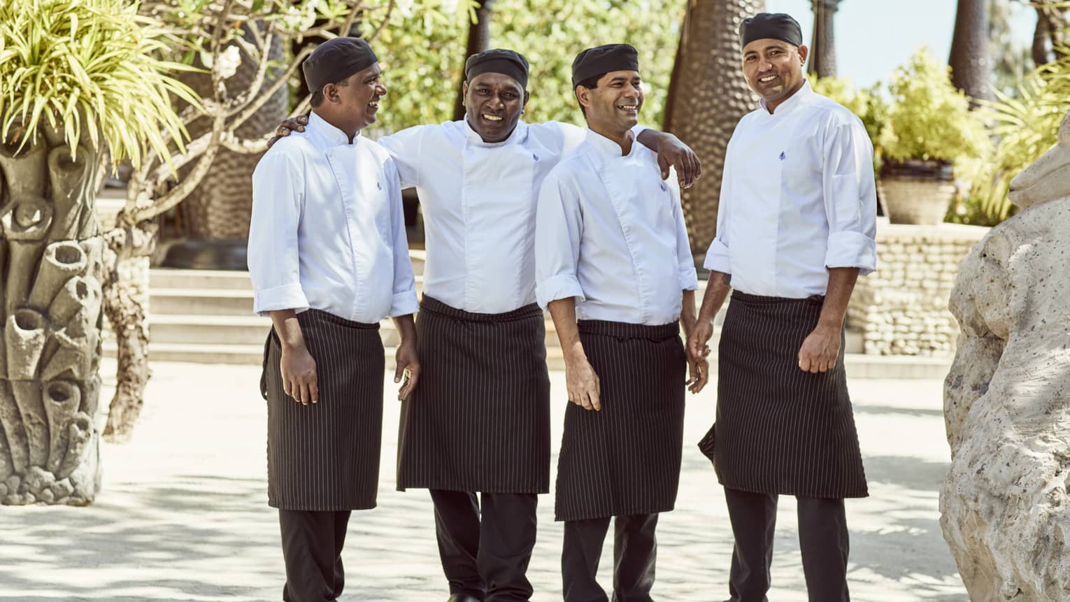 Four smiling chefs in white coats pose outdoors