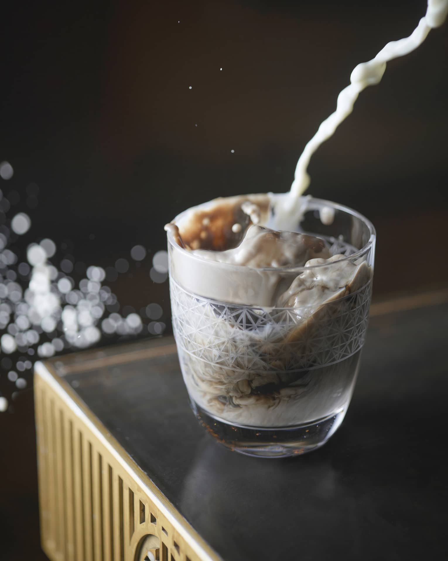 Stream of milk being poured into etched glass on dark bartop